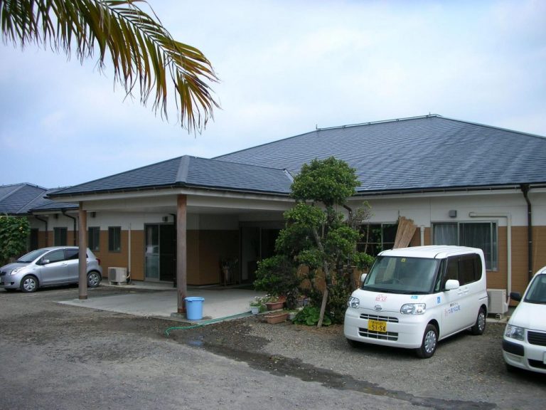 平屋建ての介護施設の建物外観。駐車場に複数の車が停められている。